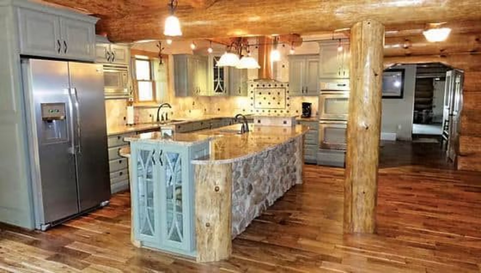 Rustic custom kitchen with stone island, timber details, and wood flooring