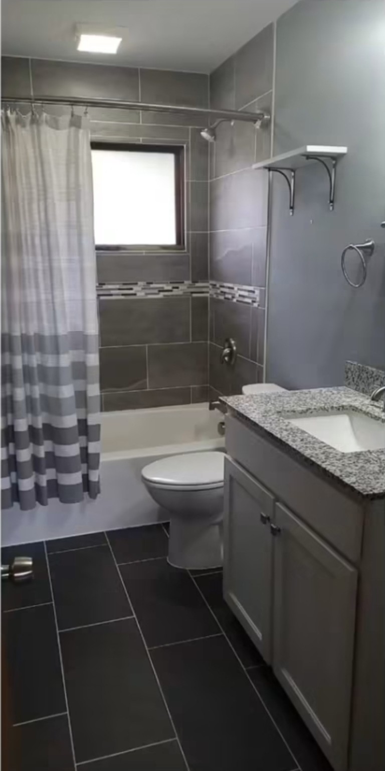 Completed gray bathroom remodel with tiled shower and granite vanity